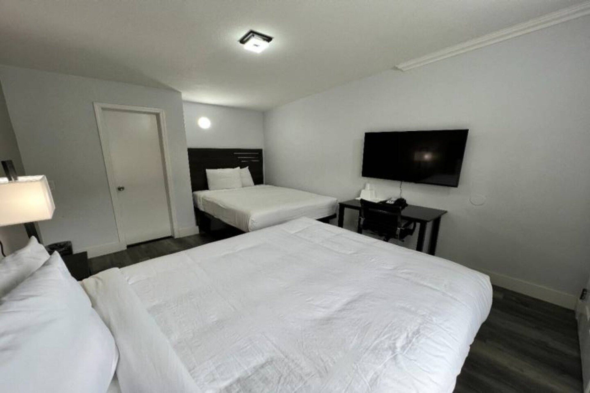 Et hotelværelse med to senge, et fjernsyn, et skrivebord og en dør.
