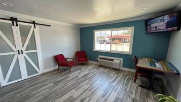 A room with a large sliding door, two red chairs, a table, a window with a view of the outside, and a mounted television.