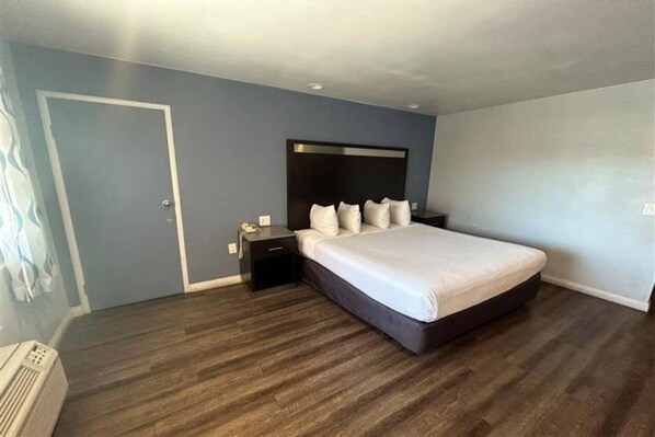A bedroom with a large bed, a nightstand, a dresser, and a door.