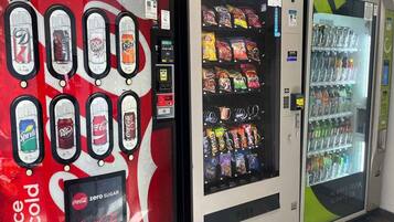 A vending machine with various beverage options, a Coca-Cola branded machine, and a refrigerator stocked with snacks and drinks.