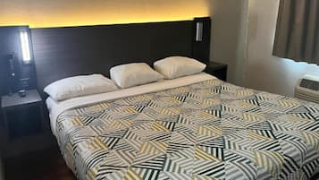 A hotel room with a bed, two bedside tables, a nightstand, a wall-mounted lamp, and a window with curtains.