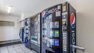 Three Pepsi vending machines in a room with tiled flooring and a wall-mounted air conditioner.