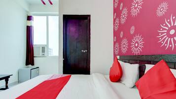 Habitación de hotel con cama, mesita de noche, ventana con cortinas, puerta y pared con un diseño de sol.