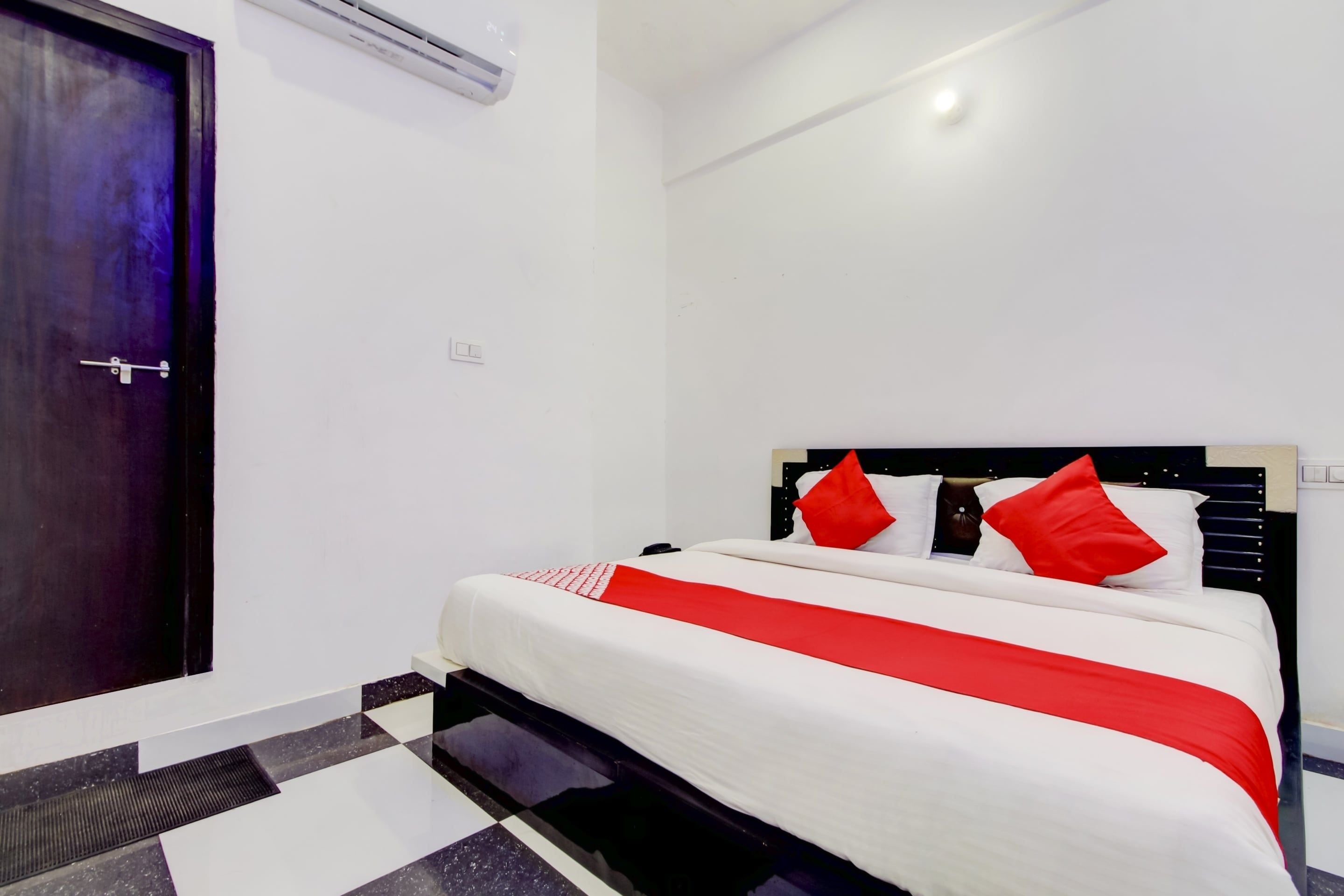 Habitación de hotel con cama, una puerta y un equipo de aire acondicionado instalado en la pared.