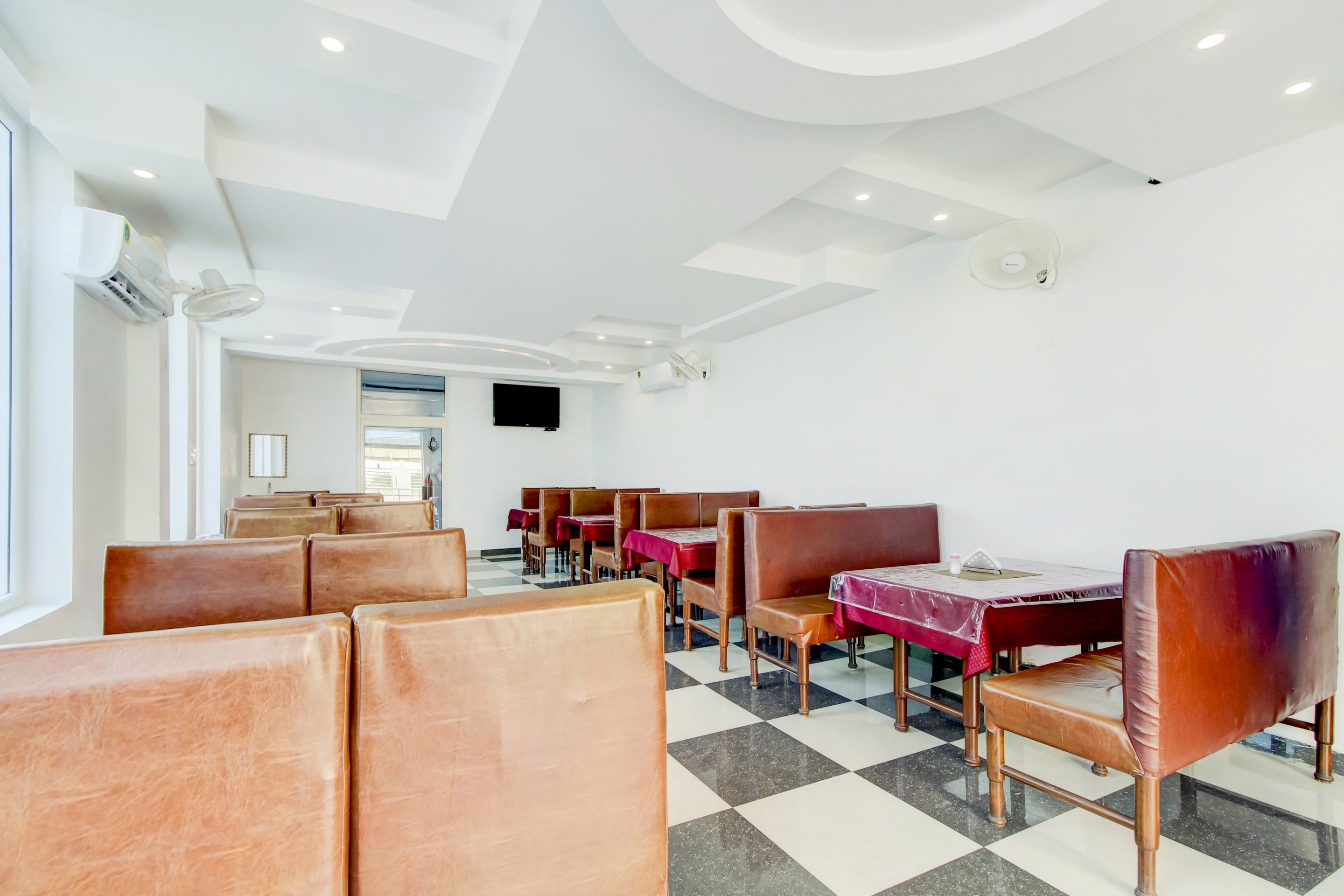 A restaurant with booths and tables, checkered flooring, and a flat-screen TV on the wall.