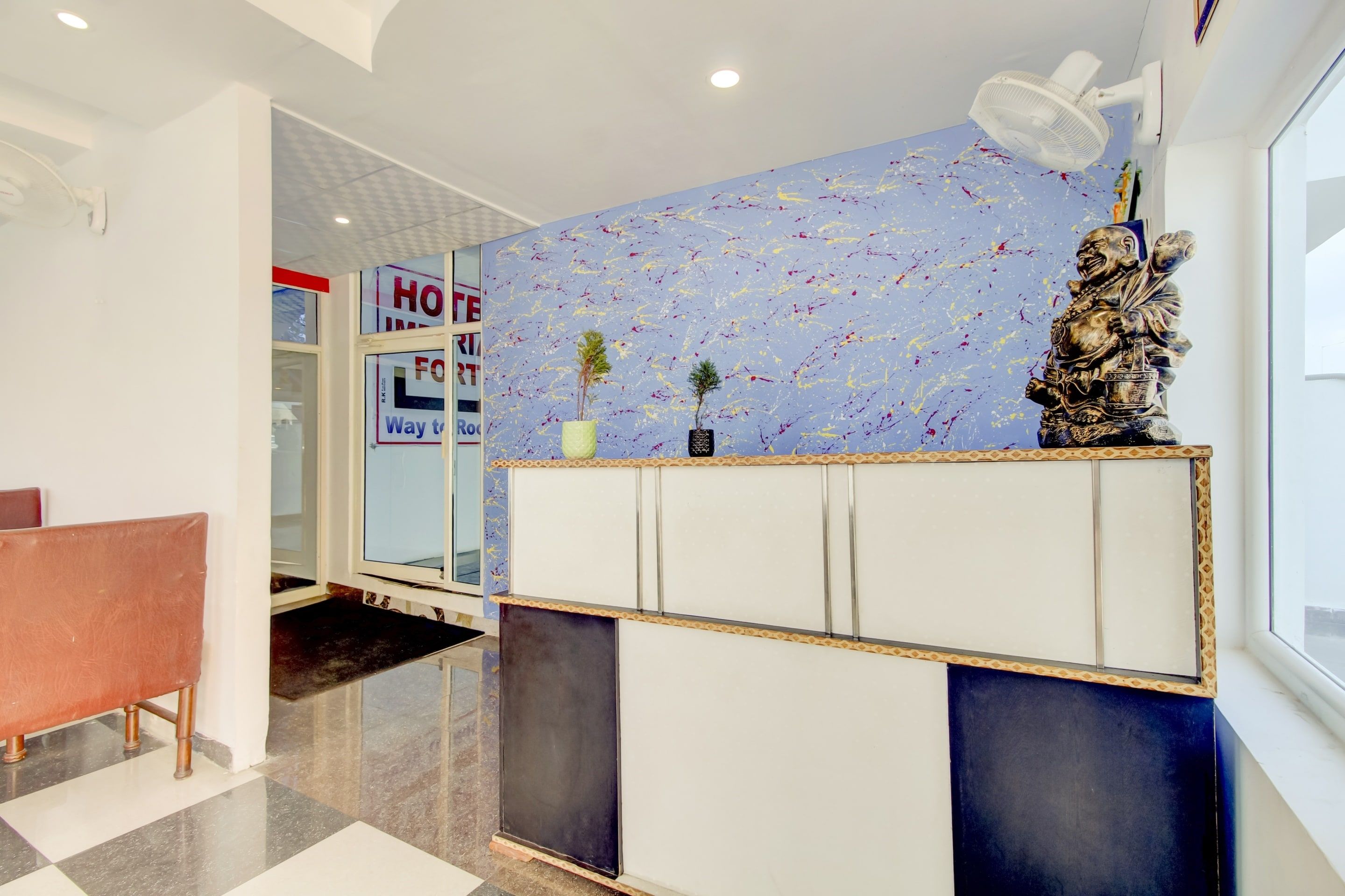 Un mostrador de recepción con una pared azul que presenta arte abstracto, una planta pequeña y una estatua.