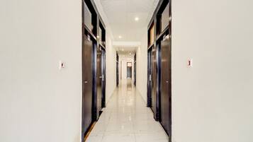 A corridor with a shiny tiled floor, flanked by dark-colored doors, leading to a bright room at the end.