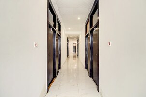 Un pasillo con piso de baldosas brillantes, bordeado por puertas de color oscuro, que conduce a una habitación luminosa al final.