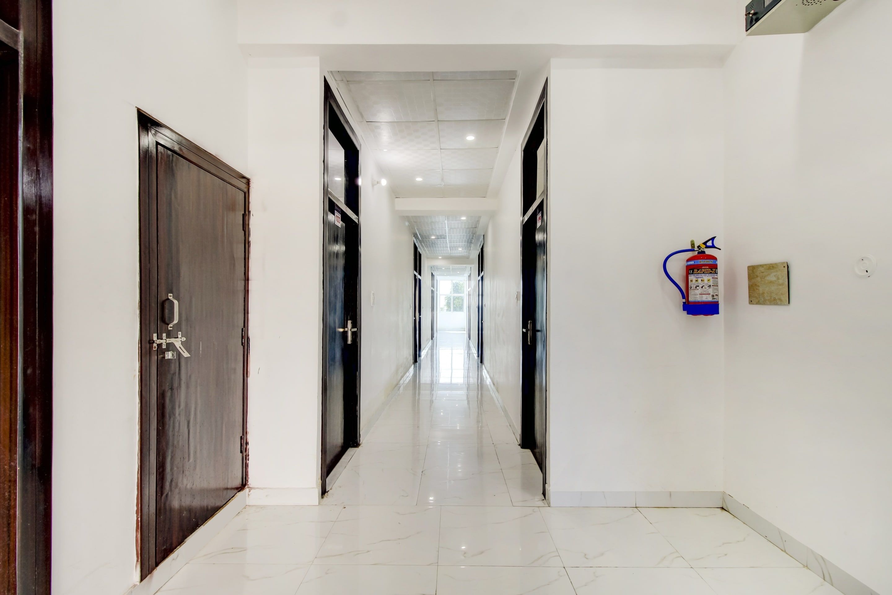 Pasillo de hotel con puertas a ambos lados, un extintor de incendios en la pared y un piso de baldosas limpio.