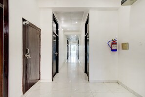 A hotel corridor with doors on both sides, a fire extinguisher mounted on the wall, and a clean, tiled floor. - Collection O New Aligarh Bus Stand (Aligarh)
