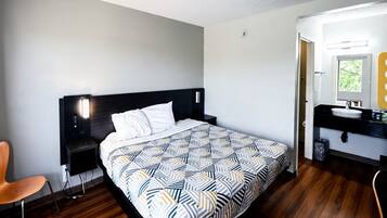 Habitació d'hotel amb llit, una vetust i una cadira, i un bany amb rentapla i mirall.