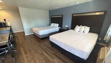 Habitación de hotel con dos camas, un escritorio con silla y una kitchenette.