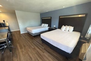 Habitación de hotel con dos camas, un escritorio con silla y una kitchenette.