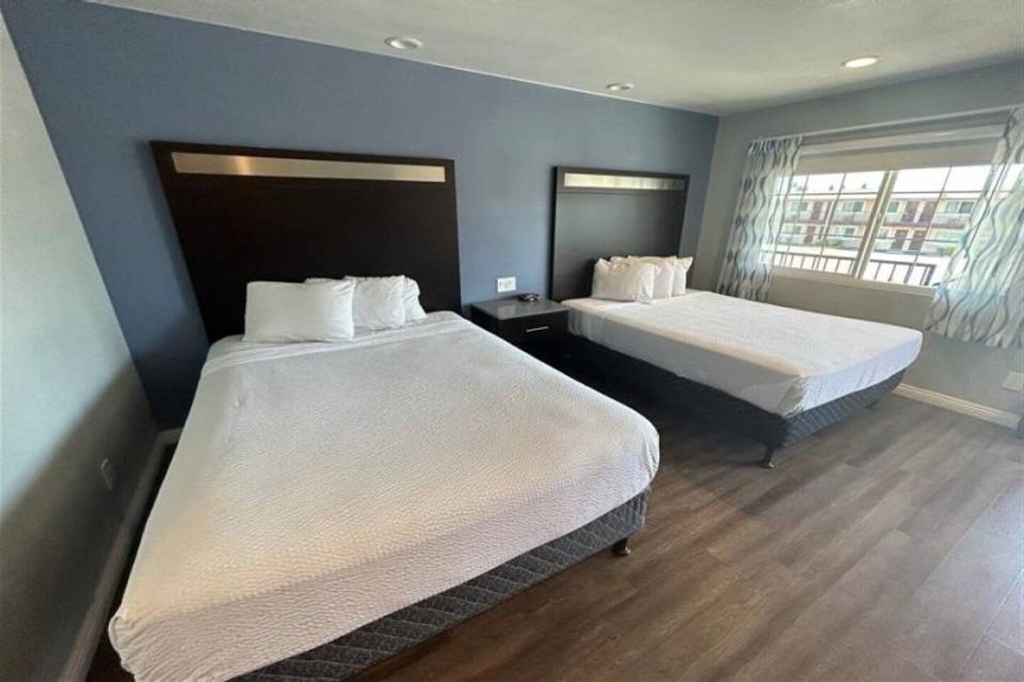 Een hotelkamer met twee bedden, een nachtkastje en een raam met gordijnen.
