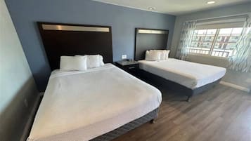 Een hotelkamer met twee bedden, een nachtkastje en een raam met gordijnen.