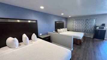 A hotel room with two beds, a desk, a chair, a microwave, and a curtain.