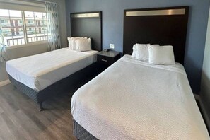 Une chambre d’hôtel avec deux lits, une table de chevet et une fenêtre avec des rideaux.