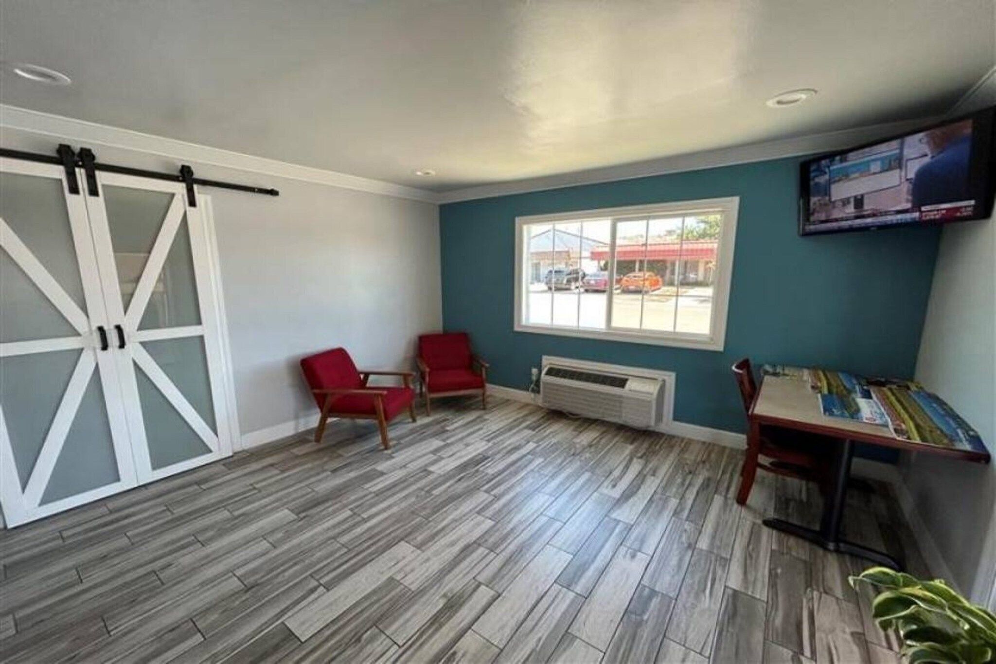 A room with a large sliding door, two red chairs, a table, a window with a view of the outside, and a mounted television.