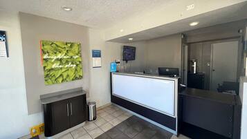 A reception area with a counter, a trash bin, a wall-mounted TV, and a framed sign.