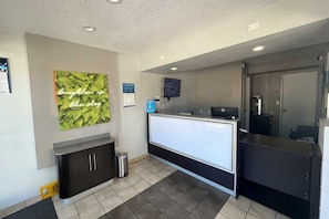 A reception area with a counter, a trash bin, a wall-mounted TV, and a framed sign. - 2 Full Beds|NS | Modesto (Modesto)