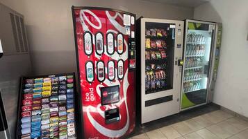 Ein Getränkeautomat mit verschiedenen Snacks und Getränken, ein Coca-Cola Automat und ein Kühlschrank mit Flaschenwasser.