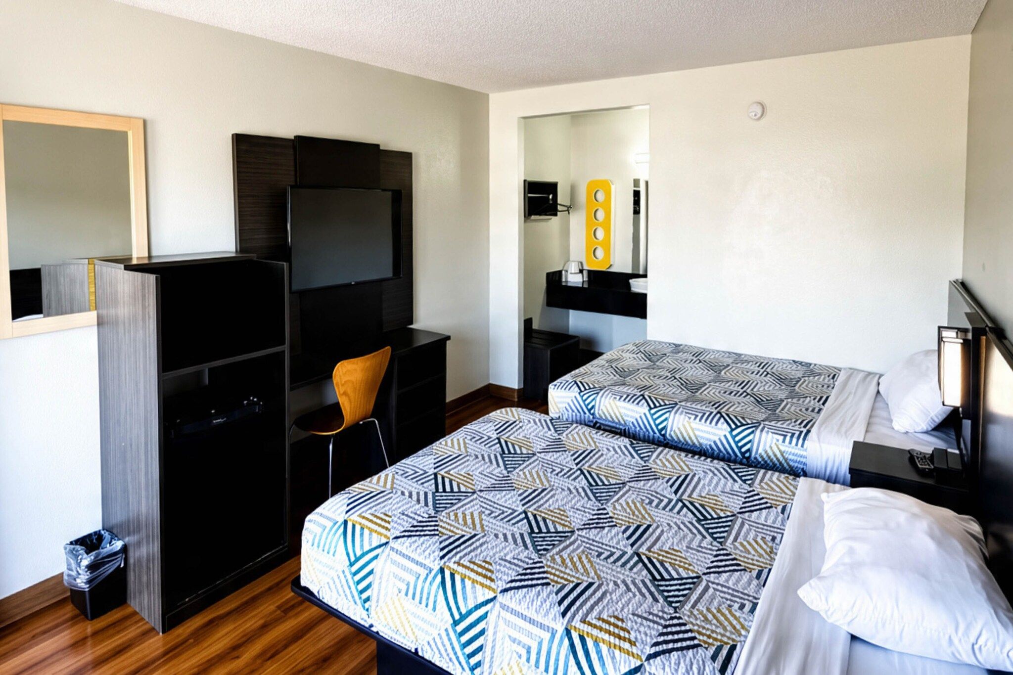 A hotel room with two beds, a desk, a chair, a television, and a mirror.