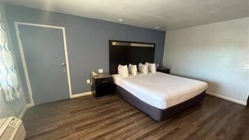 A bedroom with a large bed, a nightstand, a dresser, and a door.