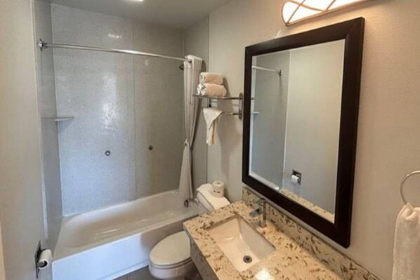A bathroom with a shower, toilet, sink, and mirror.