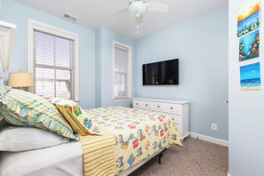 Ein Schlafzimmer mit Bett, Nachttisch, Kommode, Deckenventilator und einem an der Wand montierten Fernseher.