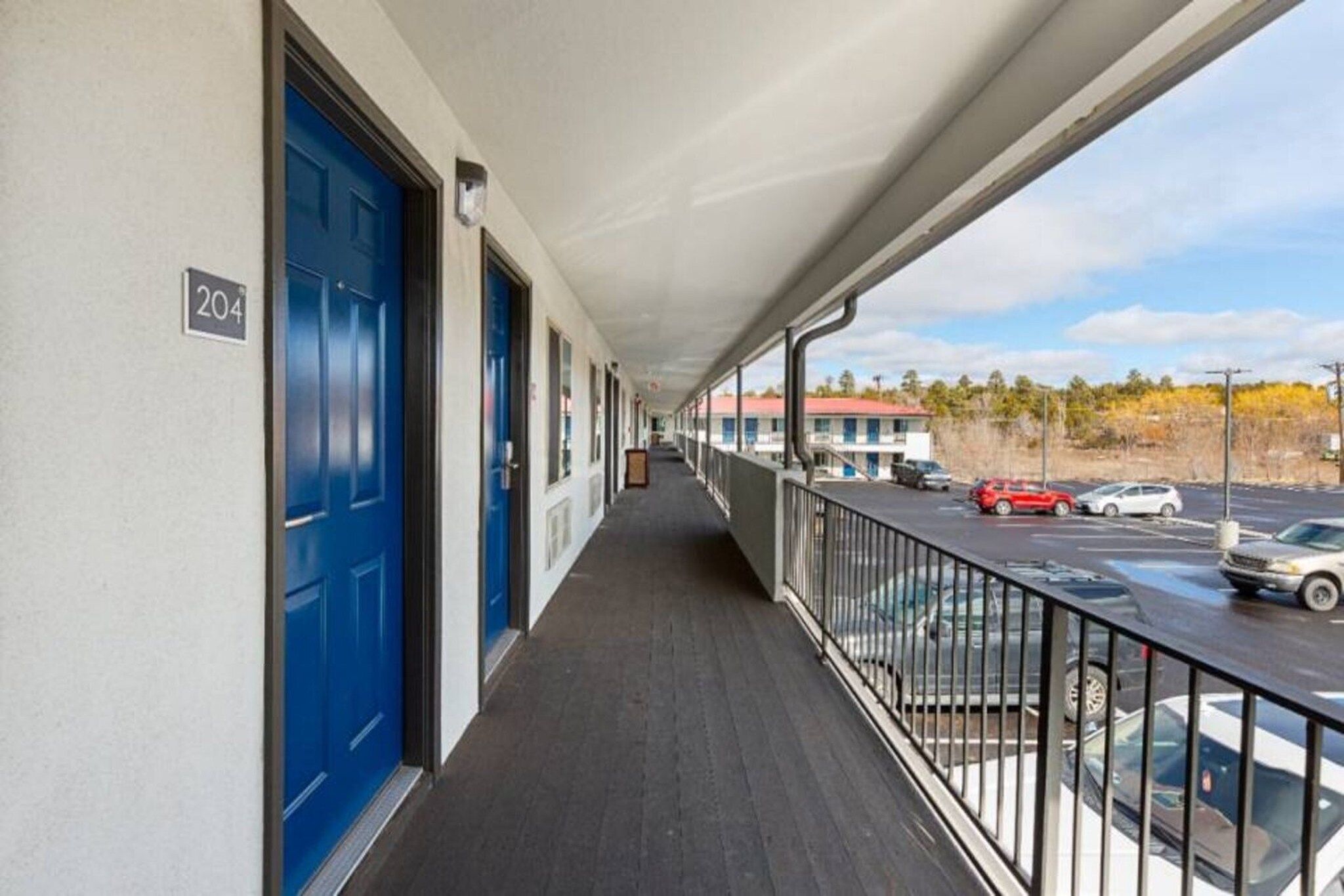 A corridor with blue doors, a balcony with a railing, and a view of a parking lot with cars.