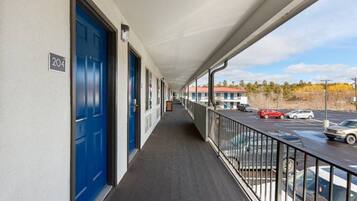 A corridor with blue doors, a balcony with a railing, and a view of a parking lot with cars.