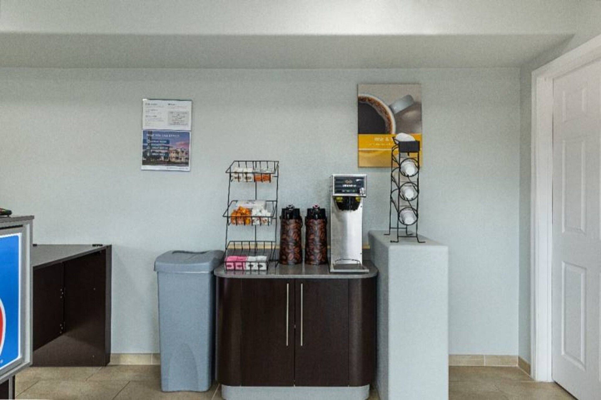 A reception area with a coffee machine, trash bin, and a bulletin board on the wall.