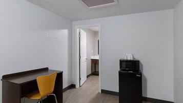 Ein Hotelzimmer mit Schreibtisch, einem Sessel, einer Mikrowelle und einer Tür zu einem anderen Raum.