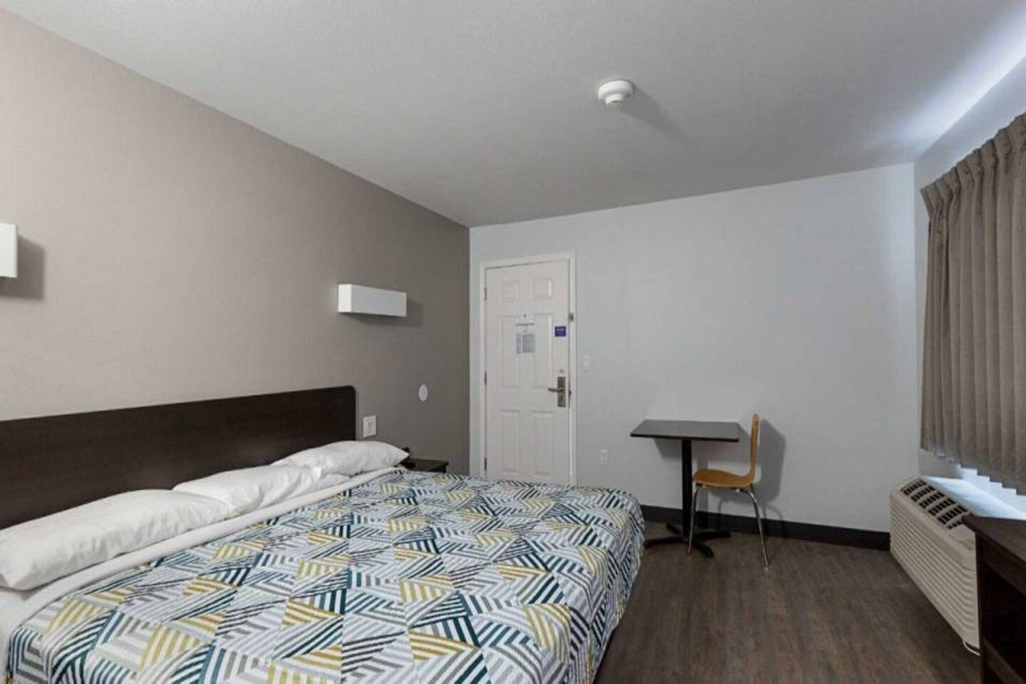 A hotel room with a bed, a desk, a chair, and a radiator.