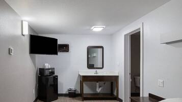 Ein Hotelzimmer mit Bett, Nachttisch, Spiegel, Waschbecken und Kühlschrank.