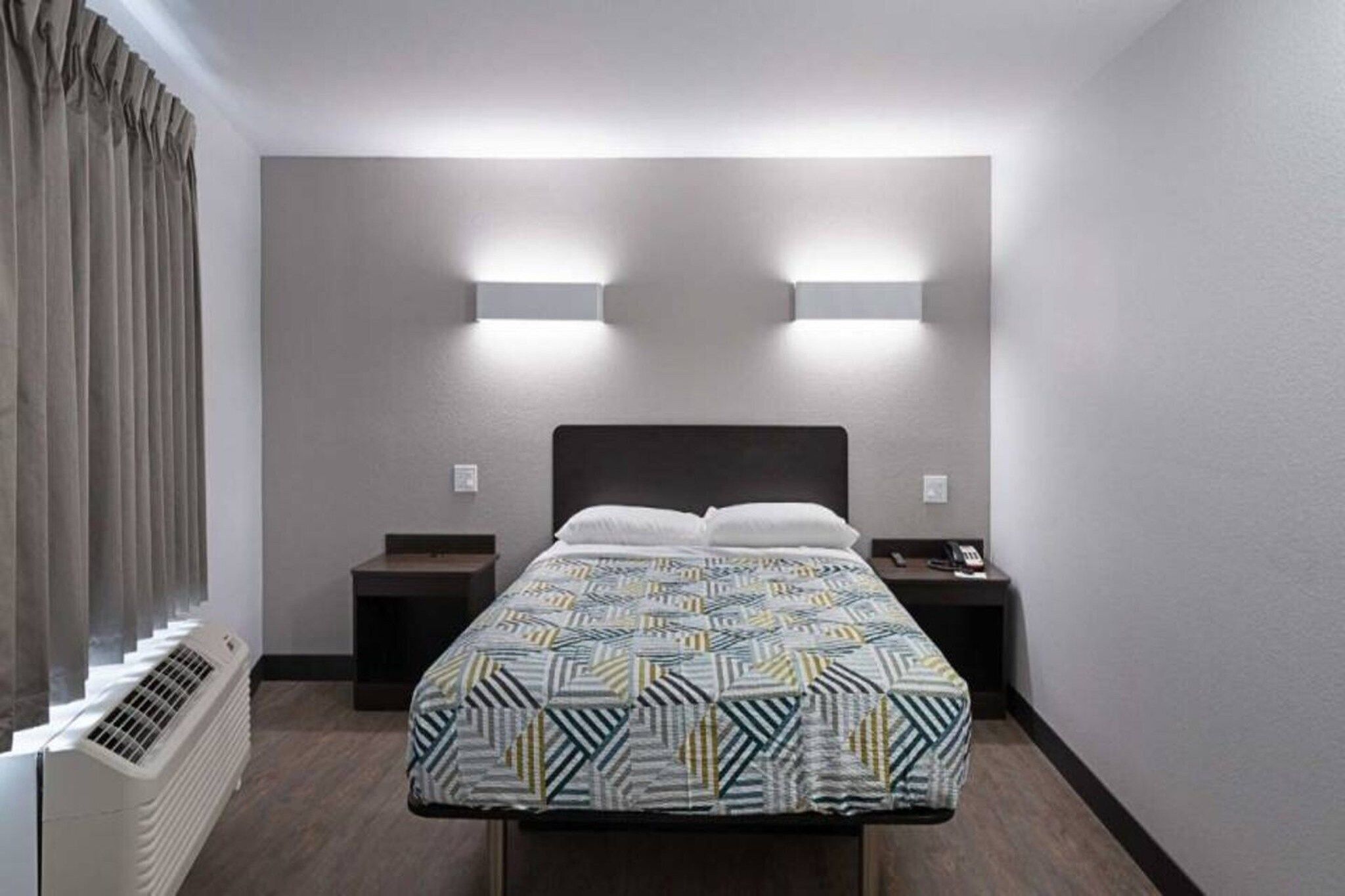 Ein Hotelzimmer mit Bett, Nachttischen, einem Heizgerät und einem fenster mit Vorhängen.