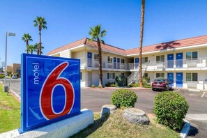 A motel sign with the number 6, a two-story building with balconies, palm trees, and a parked car.