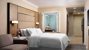 Ein Hotelzimmer mit Bett, Nachttischen, einem Sessel, einem Spiegel, einer Tür und einem Kühlschrank.