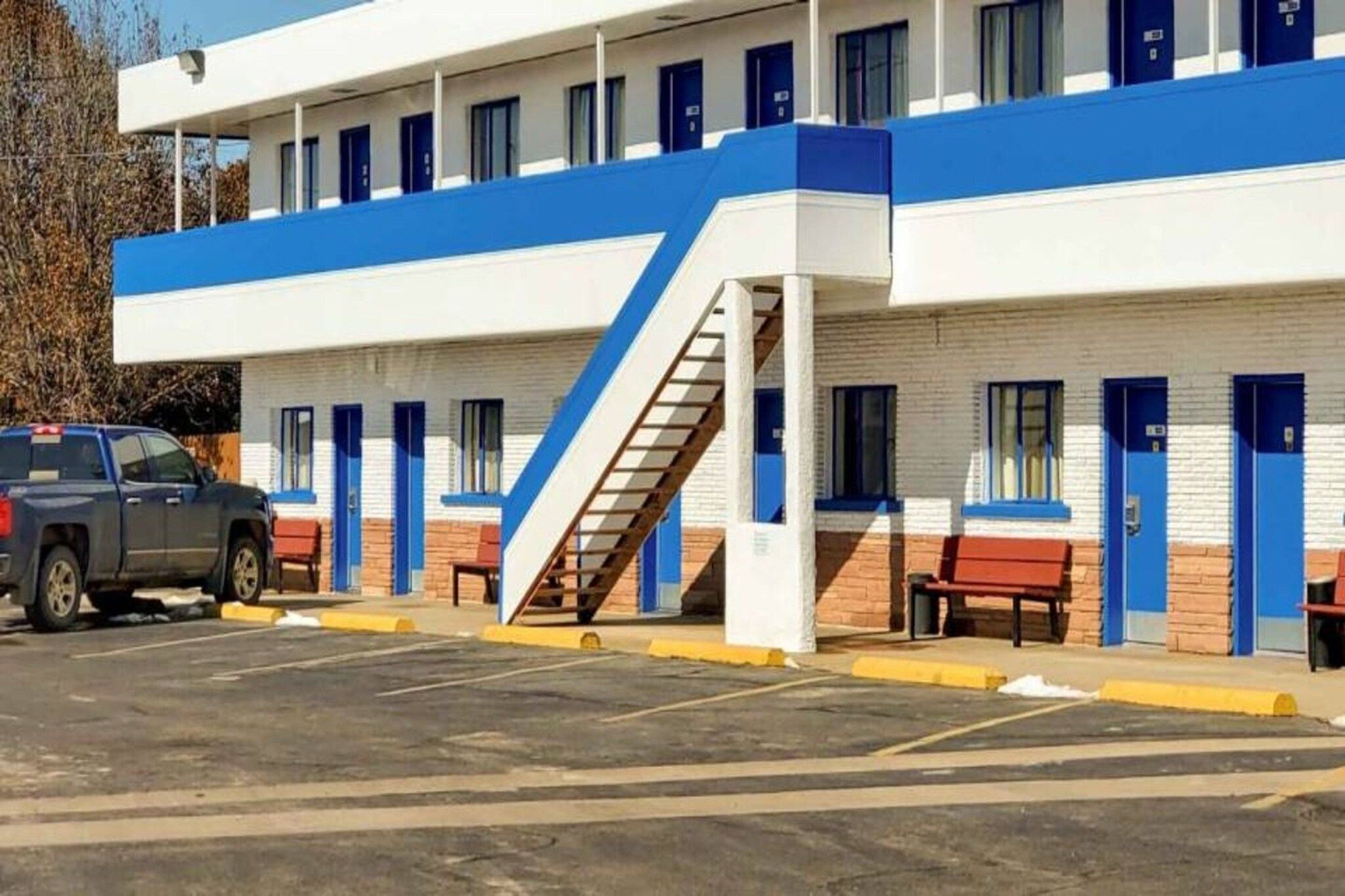 A motel with a row of rooms, a staircase, and a parking lot.