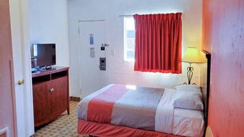A hotel room with a bed, a desk, a television, a window with curtains, and a lamp.