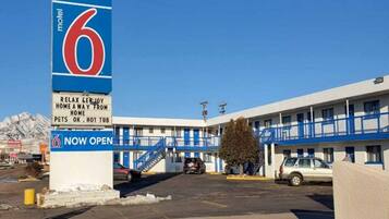 A motel with a large sign indicating it is now open, featuring a number 6 and a pet-friendly message.