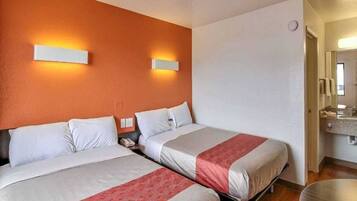 A hotel room with two beds, a small table, a chair, and a bathroom visible through an open door.