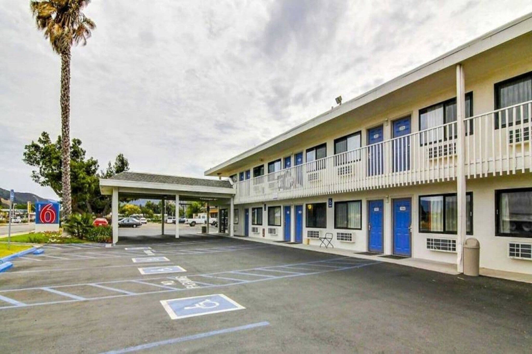 A motel with a covered parking area, multiple rooms, and a palm tree.