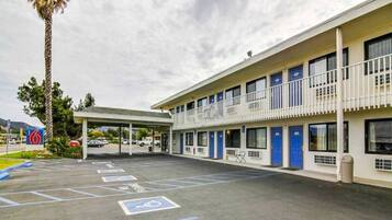 A motel with a covered parking area, multiple rooms, and a palm tree.