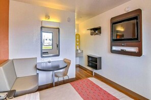Une chambre d’hôtel de taille réduite, comprenant un lit, une petite table, une chaise, un téléviseur et une fenêtre.