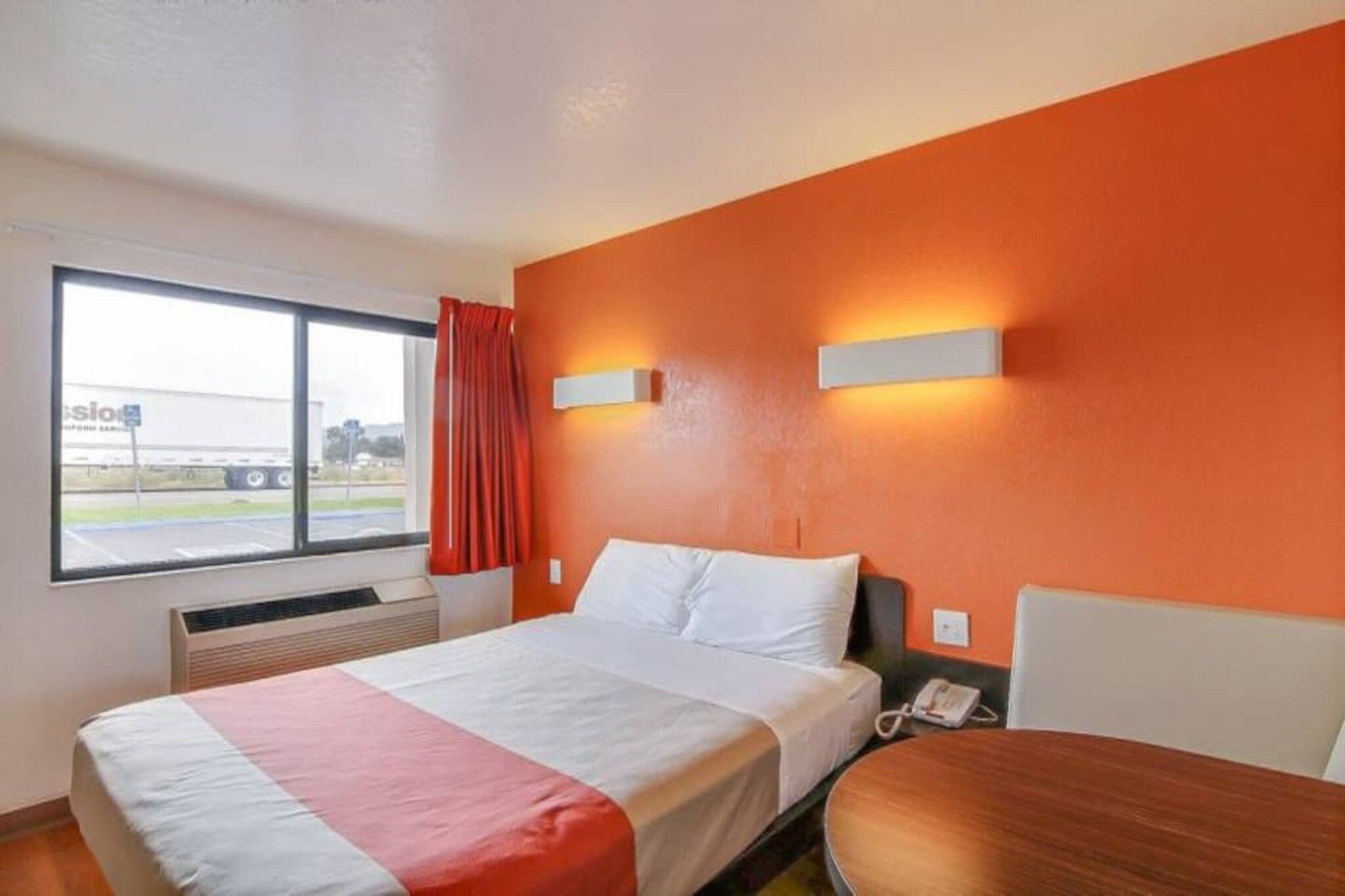 Habitación de hotel con cama, una mesa, una ventana que muestra un camión y un equipo de aire acondicionado.