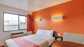 Habitación de hotel con cama, una mesa, una ventana que muestra un camión y un equipo de aire acondicionado.