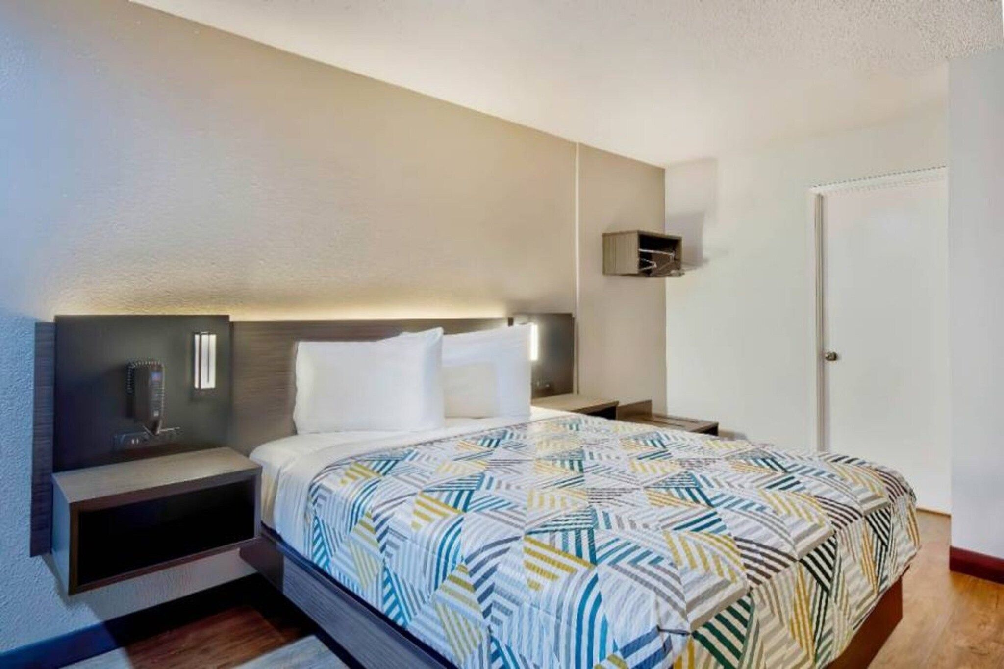 Habitació d'hotel amb un llit, taules de nit, una làmpada penjada a la paret i una porta.