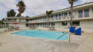 A hotel with a swimming pool, outdoor seating, and a multi-story building with balconies.