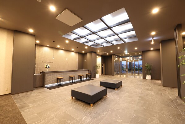 A modern lobby with a reception desk, seating area, and a glass ceiling.